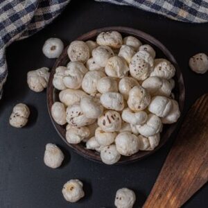 A rustic bowl filled with puffed lotus seeds on a black background, perfect for snacks.
